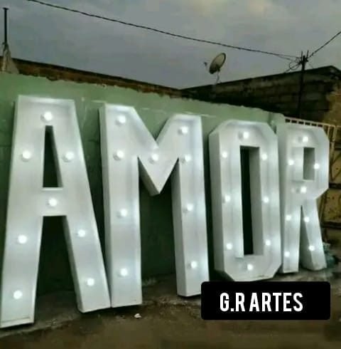 Letras grandes formando a palavra AMOR, construídas em madeira branca com pequenas luzes integradas.